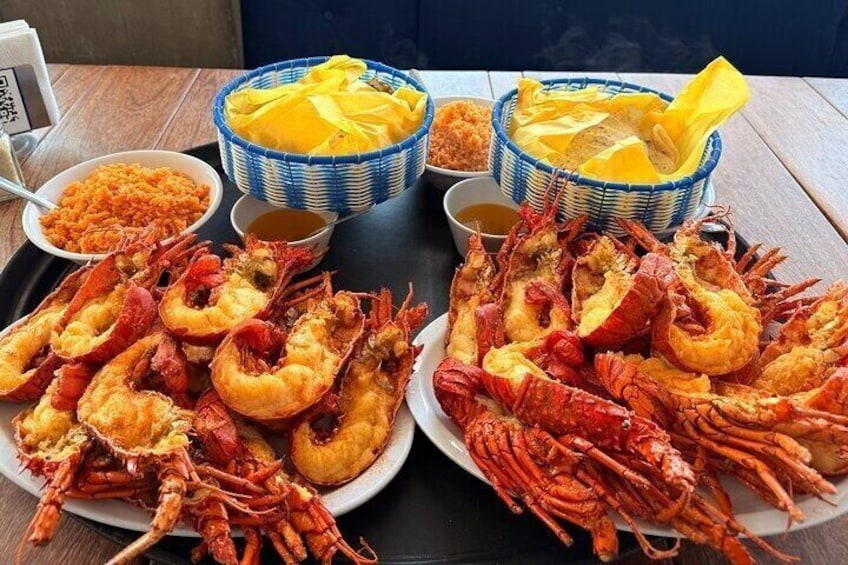 Une table avec des assiettes de fruits de mer cuits, notamment des crevettes et du homard, ainsi que des bols contenant des condiments. 1