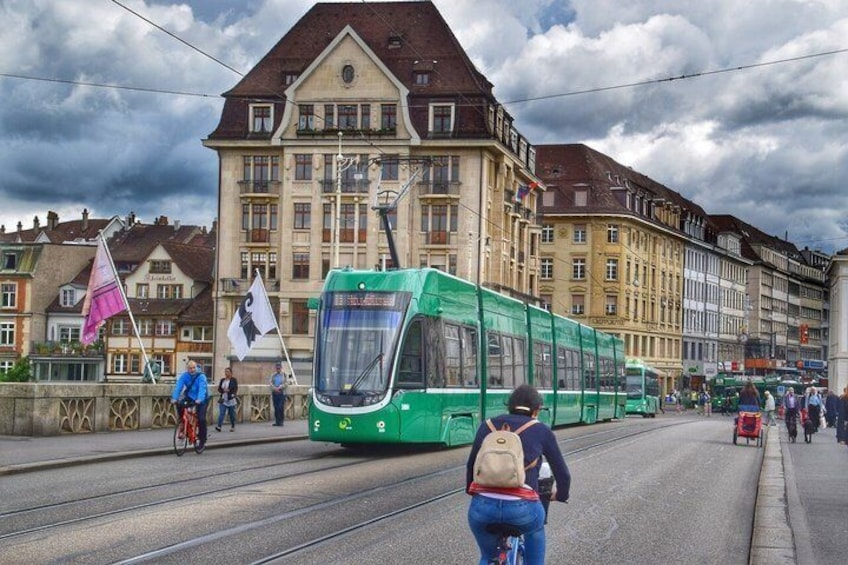 A green tram on tracks, a cyclist, and historic buildings in the background. 4