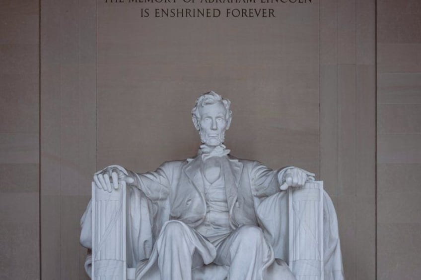 A statue of a seated man with a beard, holding a book in one hand and a flag in the other, with a plaque above stating 'THE MEMORY OF ABRAHAM LINCOLN IS ENSHRINED FOREVER.' 2