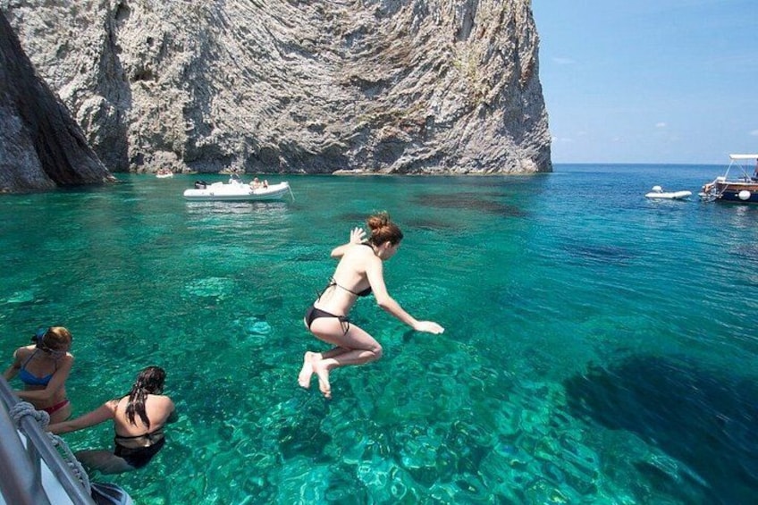 Una persona salta a unas aguas azules y transparentes, con barcos al fondo. 1