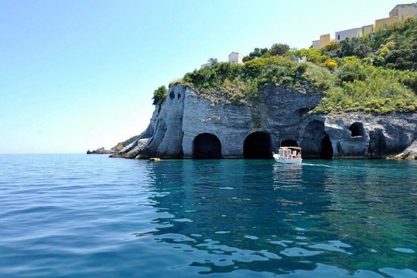 A coastal cliff with caves and a boat on the water. 4