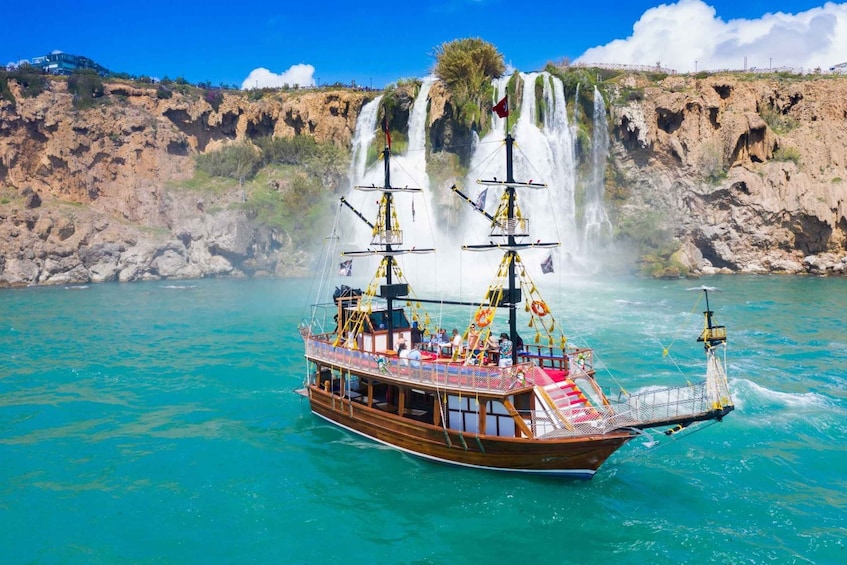 A wooden boat with a flag, sailing near a waterfall. 1
