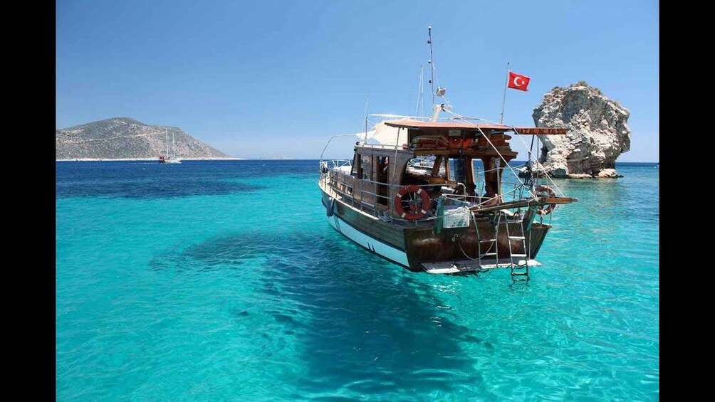 A boat anchored near a rocky coastline with clear turquoise water and a flag. 5