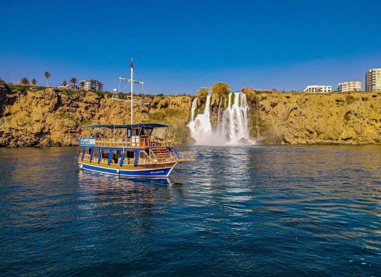 A boat named 'ATLANTIC' on calm waters, a waterfall in the background, and buildings on a hillside. 3