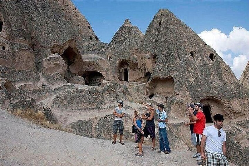 A group of people standing in front of rock formations with cave-like structures. 2