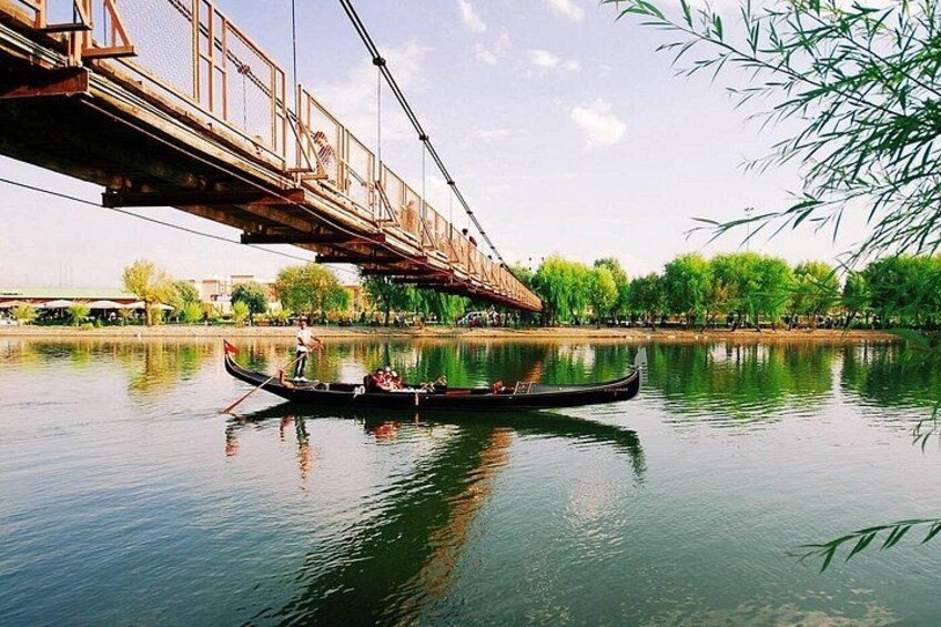 A calm river with a bridge, a boat with passengers, and lush greenery. 3