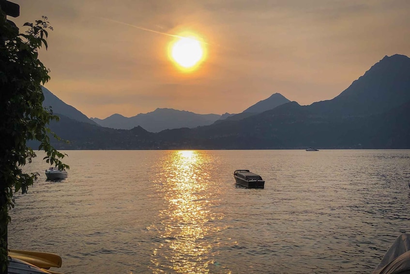 A calm lake with boats, mountains in the background, and a bright sun reflecting on the water. 5