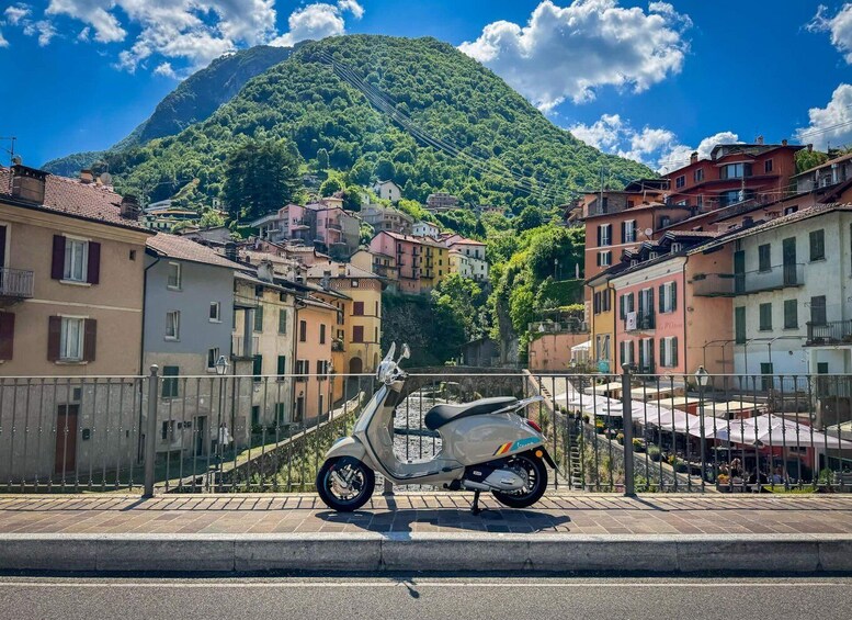 A scooter parked on a street with colorful buildings and a mountain in the background. 1