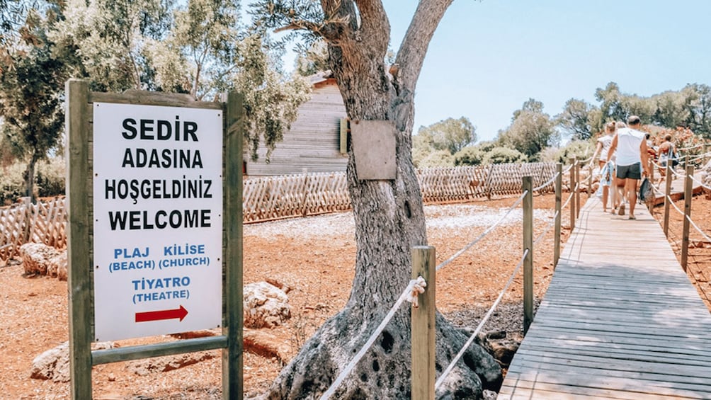 A signboard with 'SEDİR ADASINA HOŞGELDİNİZ WELCOME' and directional arrows to 'PLAJ KİLİSE (BEACH) (CHURCH)' and 'TIYATRO (THEATRE)'. 5