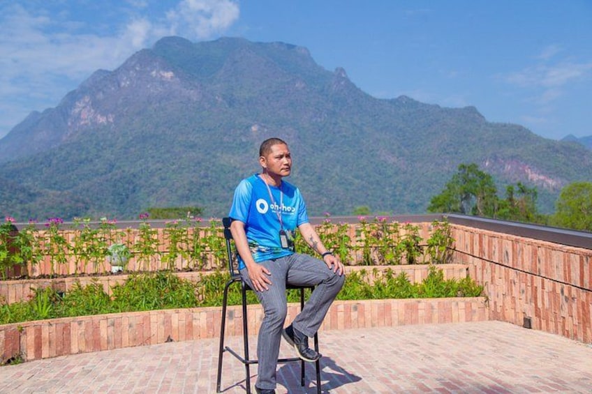 A person sitting on a chair with a mountainous landscape in the background. 1
