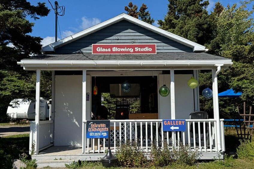 A small building with a sign reading 'Glass Blowing Studio' and a 'Gallery' sign. 3
