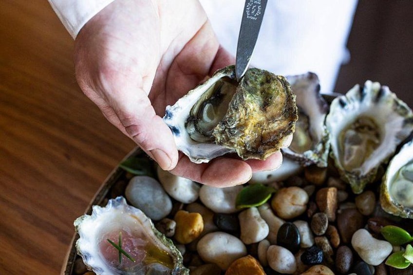 A person holding an oyster with a knife, surrounded by other oysters and pebbles. 3