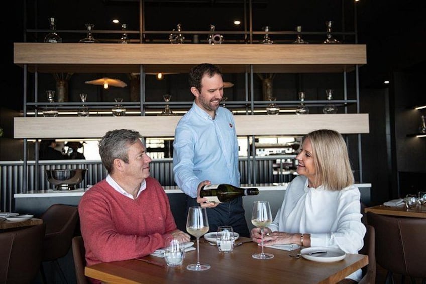 A restaurant interior with a waiter serving wine to a seated couple. 2