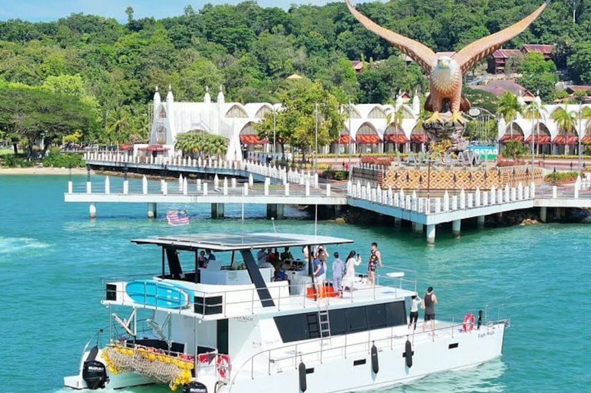 Un bote sobre aguas tranquilas, una gran escultura de ave y un edificio blanco con techo a dos aguas. 1