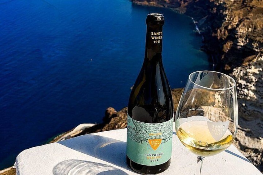 En flaska vin från Santorini och ett glas på ett bord med utsikt över kusten. 3