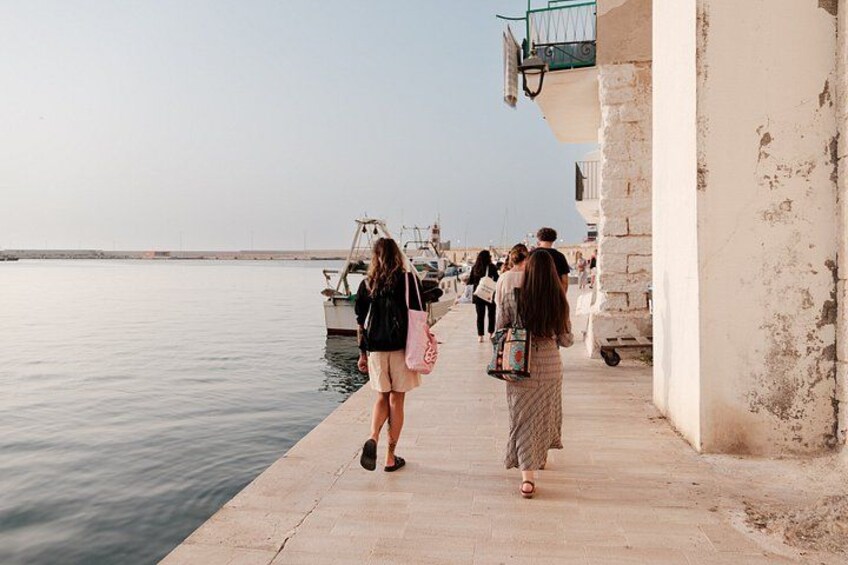 A waterfront promenade with people walking, a calm sea, and boats in the background. 4