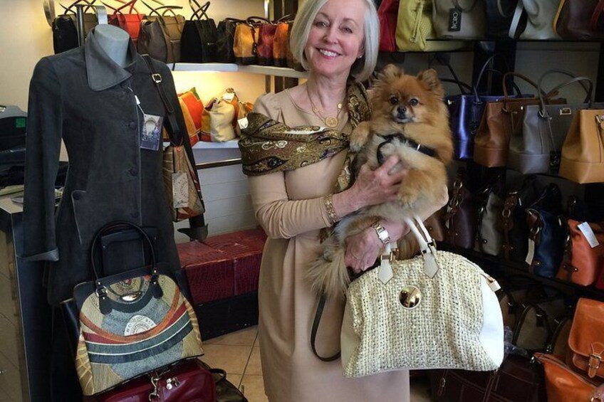 Une personne tenant un petit chien et un sac à main dans un magasin où divers sacs sont exposés. 1