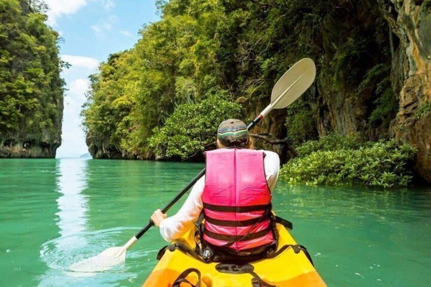A person kayaking down a narrow river surrounded by lush greenery and rocky cliffs. 3