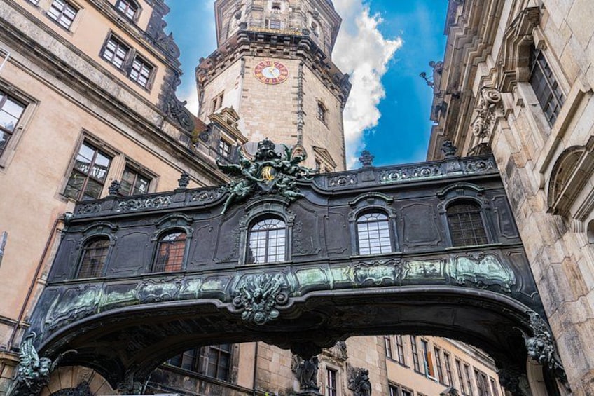 Een historische stenen brug met versierde metalen details en een klokkentoren op de achtergrond. 2
