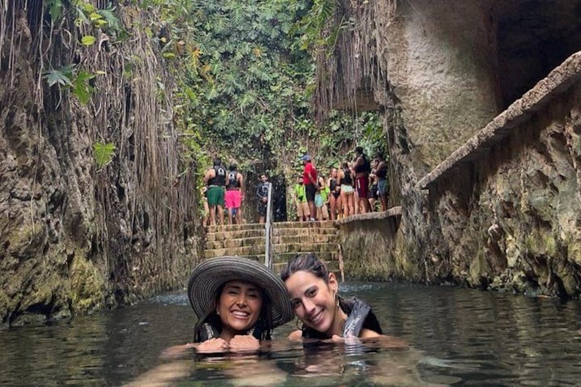 A natural pool surrounded by rocky cliffs with people standing on a stone platform. 4