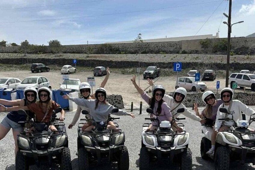 Un gruppo di persone su quad in un parcheggio, con auto e un muro di pietra sullo sfondo. 4