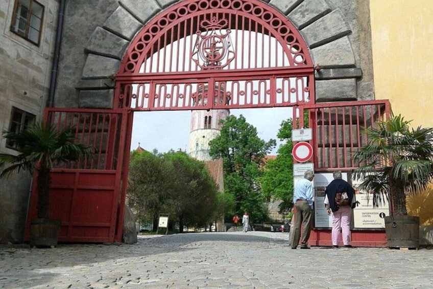 A red gate with a coat of arms, cobblestone street, and a building with a clock tower in the background. 5