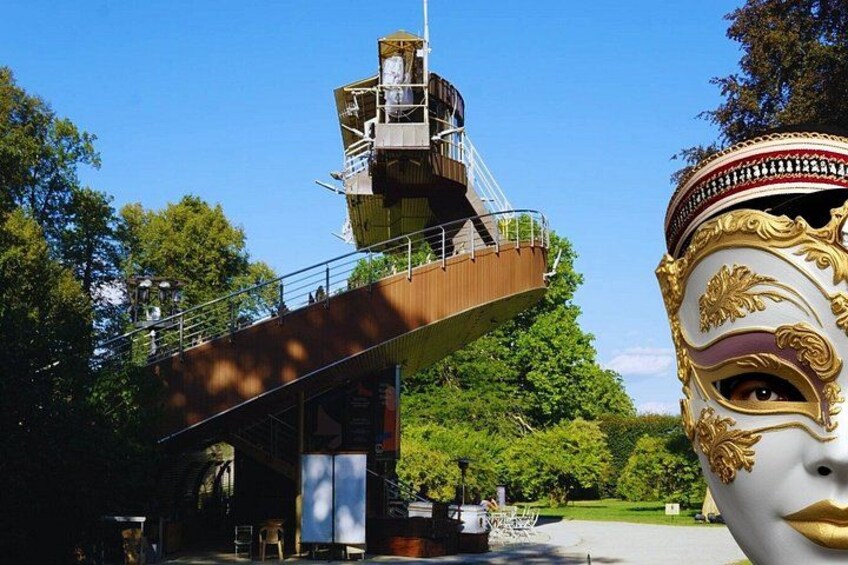 A bridge with a viewing platform, a large decorative mask, and trees in the background. 3