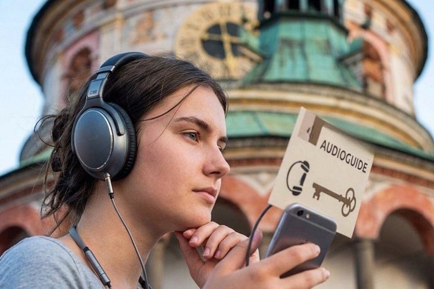 A person wearing headphones and holding a smartphone with an audioguide sign. 1