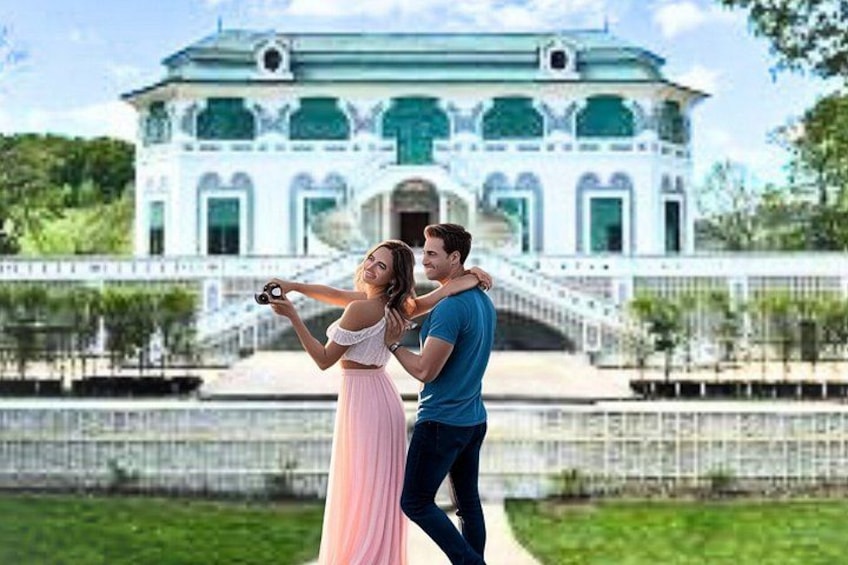 A couple taking a photo in front of a large, ornate building with a staircase leading to a green roof. 2