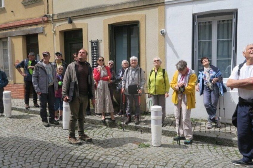 En grupp människor står på en kullerstensgata, några av dem har vandringsstavar, framför en byggnad med en skylt där det står ”CLO”. 5