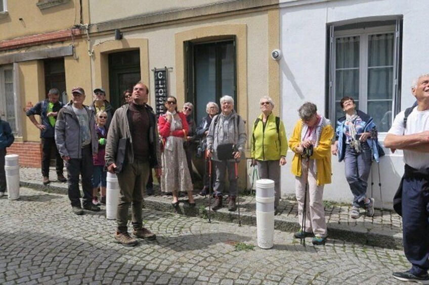 En gruppe mennesker står på en brostensbelagt gade, nogle med vandrestave, foran en bygning med et skilt der står 'CLO'. 3