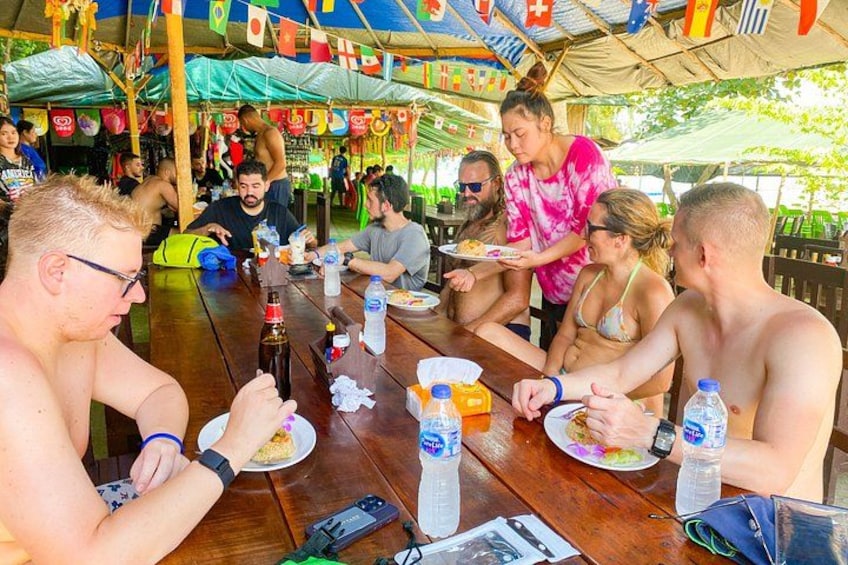 A group of people dining at an outdoor table with various food items and drinks. 4