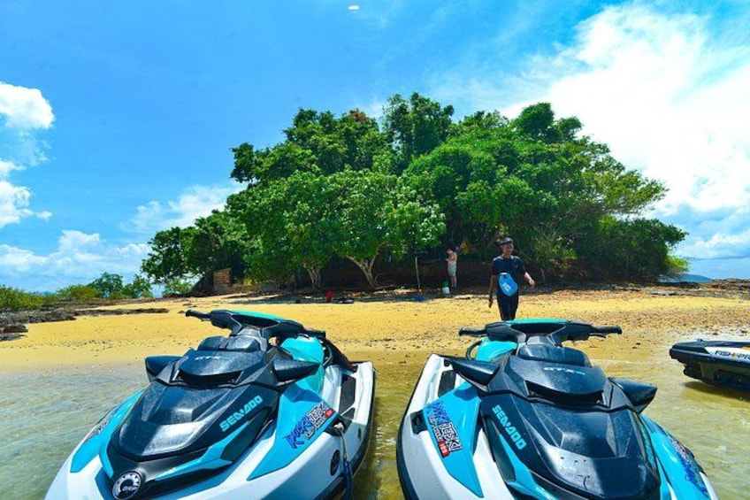 Two jet skis on a sandy beach with a person walking in the background. 3