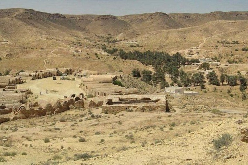 A desert landscape with ancient ruins, scattered vegetation, and distant hills. 5