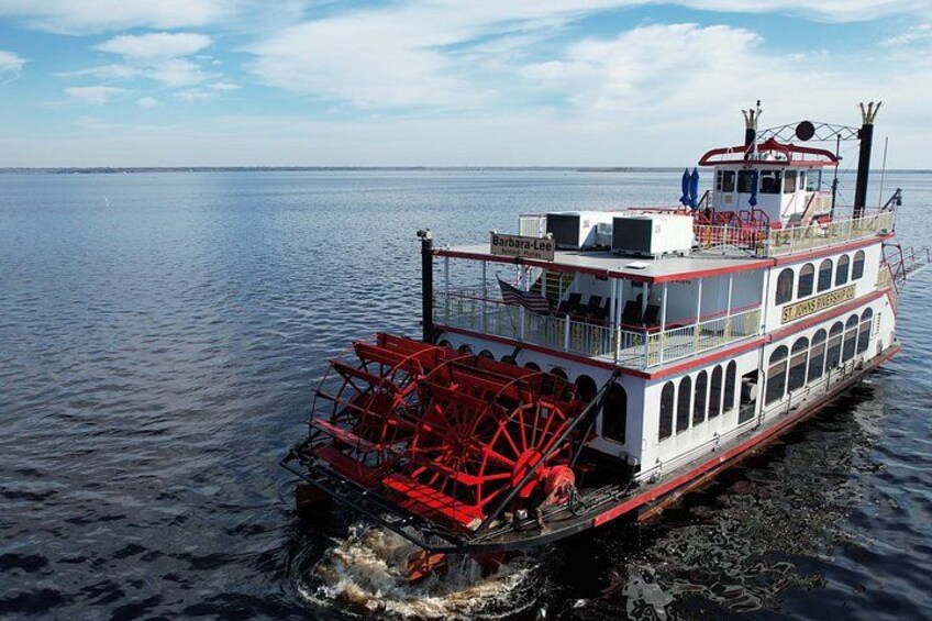 A steamboat with a large red paddle wheel on a calm body of water. 1