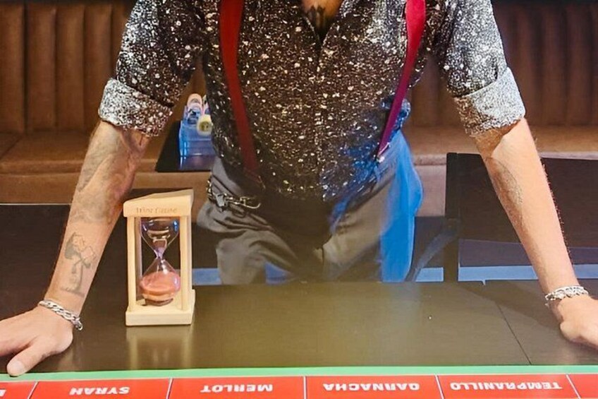 A person wearing a sparkly top with a red strap, standing behind a table with a timer and a red tablecloth with text. 3