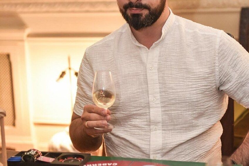 A person holding a wine glass in a room with a table that has various items on it. 5