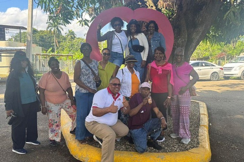 A group of people posing in front of a heart-shaped structure with a tree in the background. 3