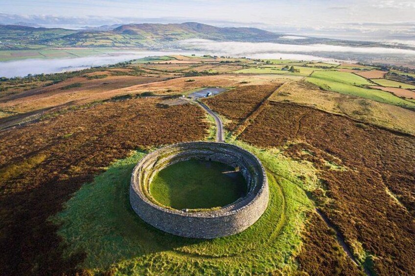 A circular stone structure surrounded by a grassy field, with a road leading to it. 3