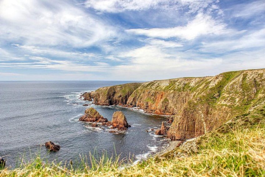 A coastal landscape with cliffs, rocky outcrops, and a grassy foreground. 2