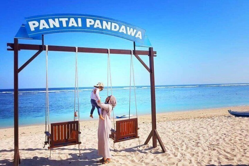 A swing set with a sign reading 'PANTAI PANDAWA' on a beach. 1
