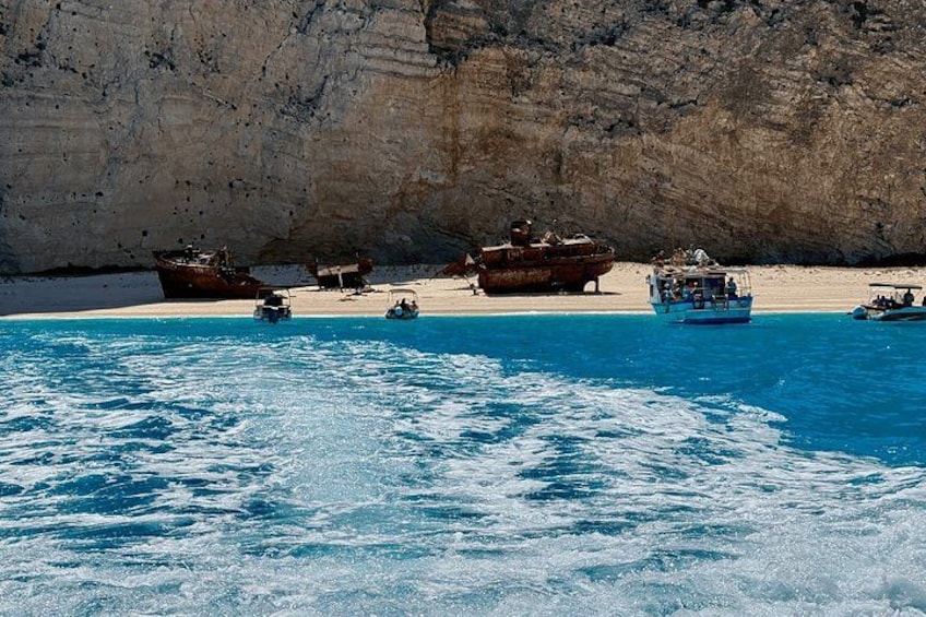 A coastal scene with clear blue water, boats, and a rocky cliff. 1