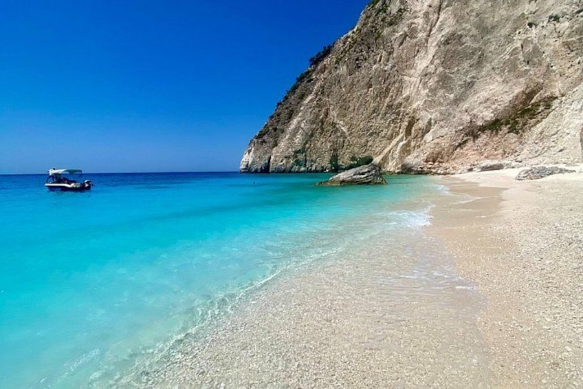A beach with clear turquoise water, a rocky cliff, and a boat in the distance. 5