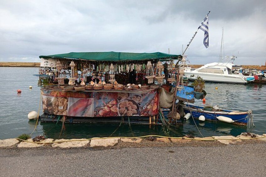 Een drijvende marktstand met diverse waren, een aangemeerd bootje en een rustig waterlichaam. 4