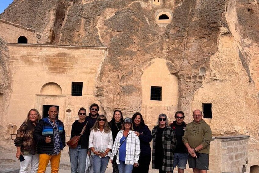 A group of people standing in front of a historic stone building with arched windows and a rugged exterior. 4