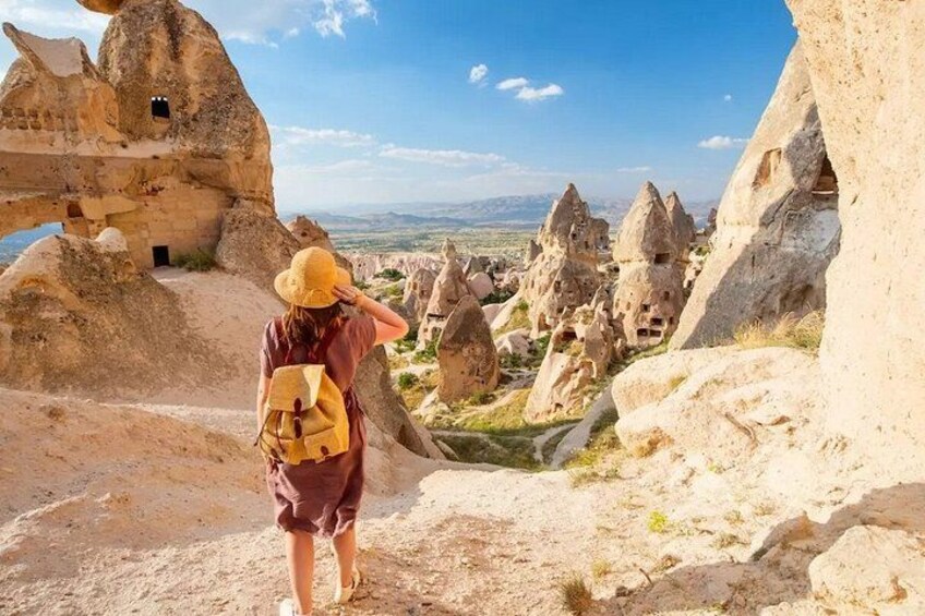 A person with a backpack and hat standing on a rocky terrain with unique rock formations and a distant view of a landscape. 1