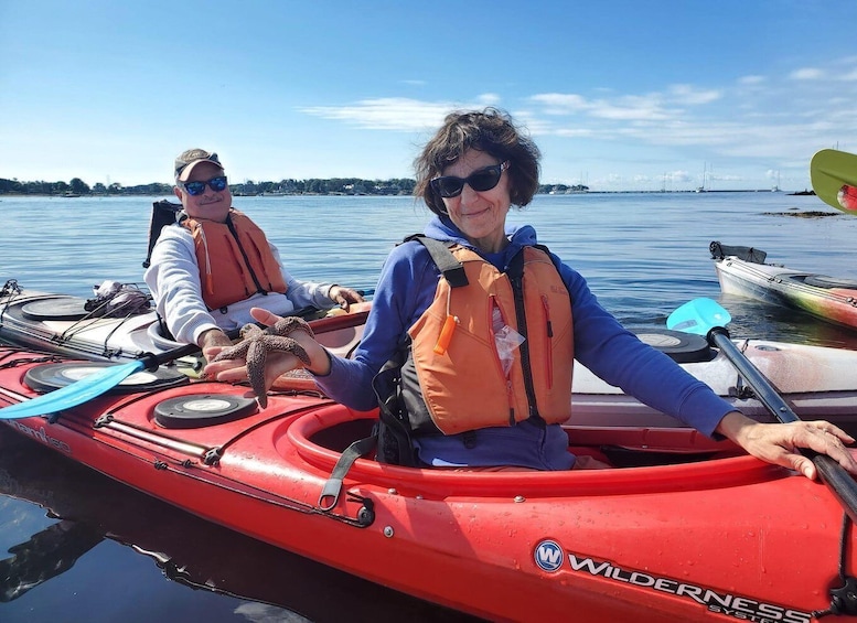 Two people in a red Wilderness kayak on calm water with a clear sky. 1