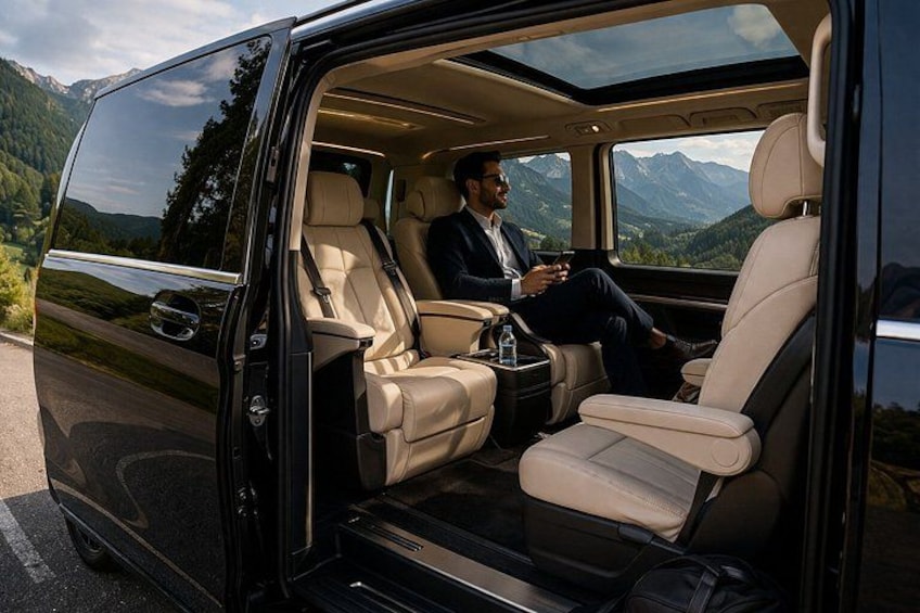 Un furgone di lusso con un uomo seduto sul sedile posteriore, un tetto apribile e una vista panoramica sulle montagne. 1