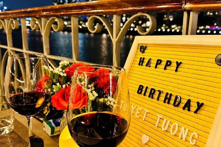Een tafel met twee glazen rode wijn, rode rozen en een geel bordje waarop 'HAPPY BIRTHDAY' staat. 4