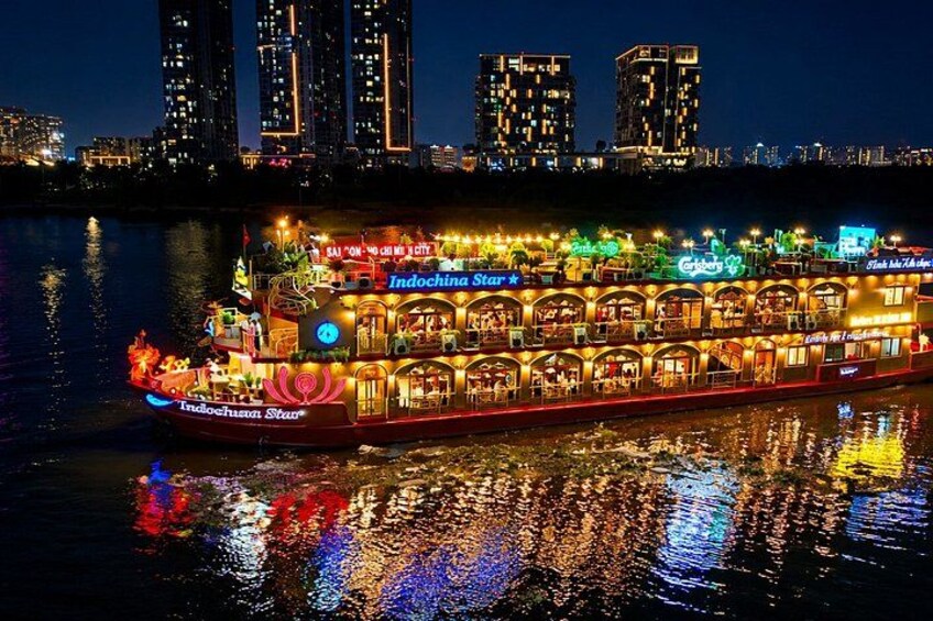 Een fel verlichte riviercruiseschip met meerdere dekken en verlichte borden, met reflecties op het water. 5